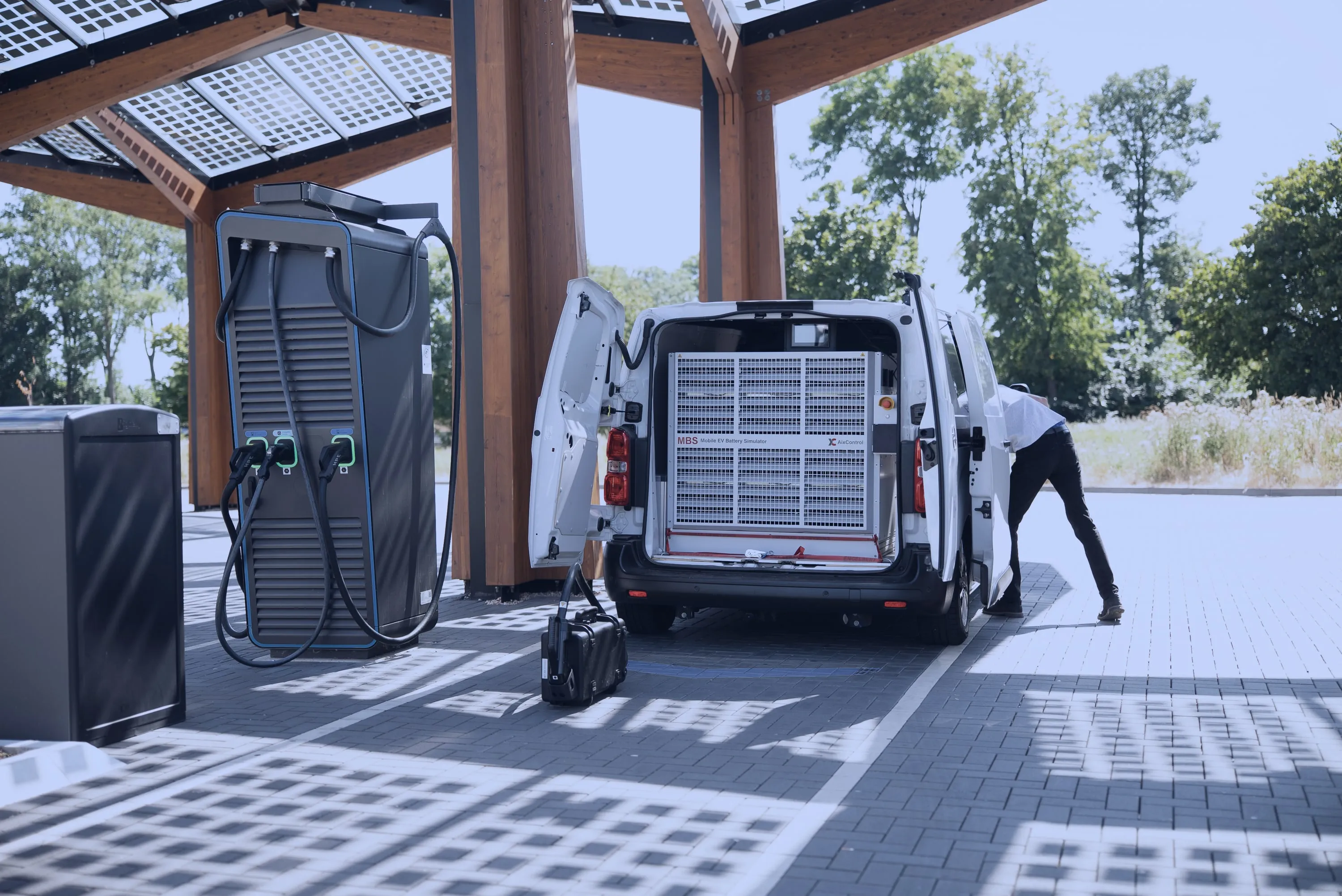 Charging park with six DC fast charging points at sunrise, two AixCalibration service vans alongside